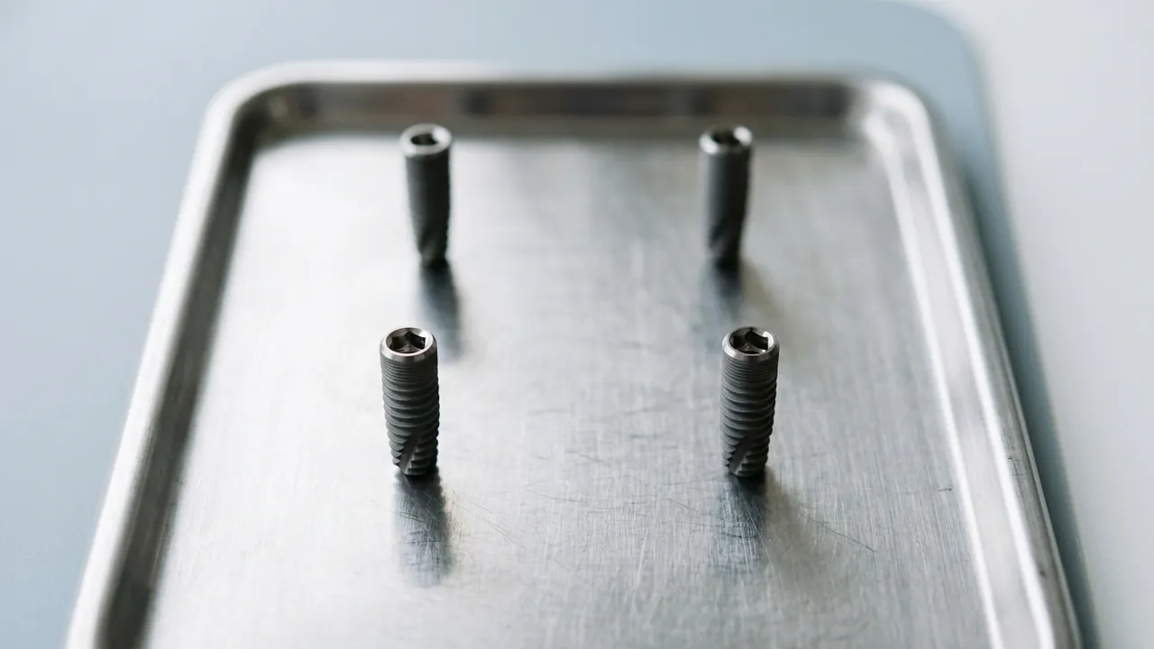 Four titanium dental implant posts standing upright at the corners of an invisible square on a brushed stainless-steel tray — All-on-4 dental implants