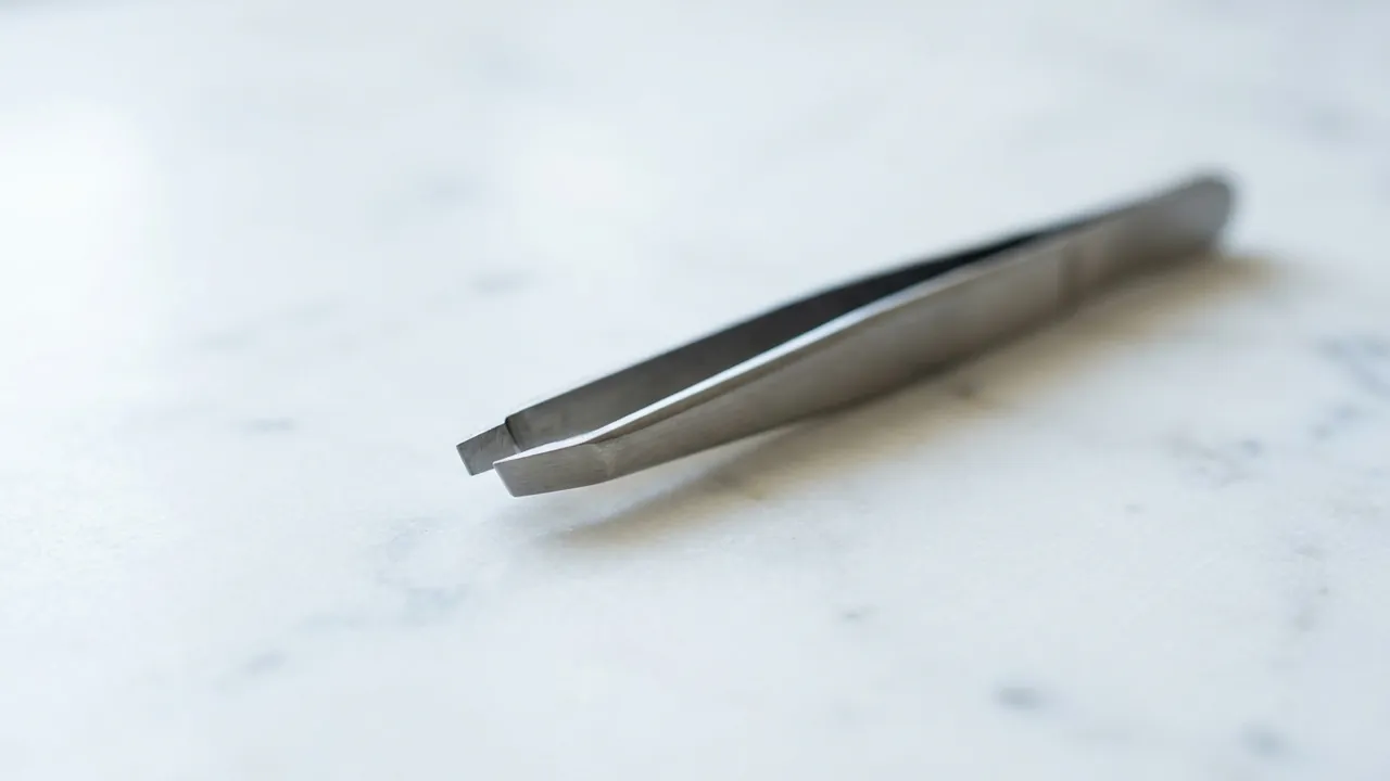 A slanted steel tweezers lying diagonally on white marble — Brow lift